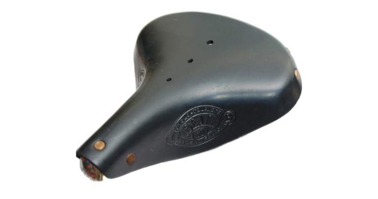 A black Idéale TB 60 Cyclo-Touriste saddle in three quarter view, its embossed oval and three vent holes visible over copper rivets at the nose