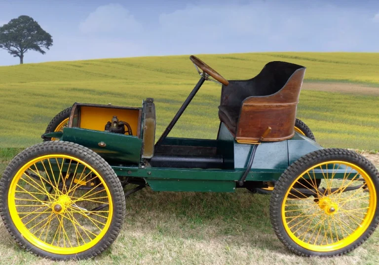 A restored 1904 F. Tron et Cie runabout photographed in a field, its green body and wooden bucket seat set on bright yellow wire wheels