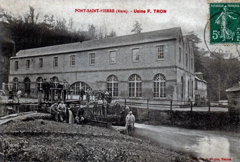 Postcard captioned Pont-Saint-Pierre, Usine F. Tron, showing the long brick and stone factory beside its millrace with about twenty workers posed along the bank