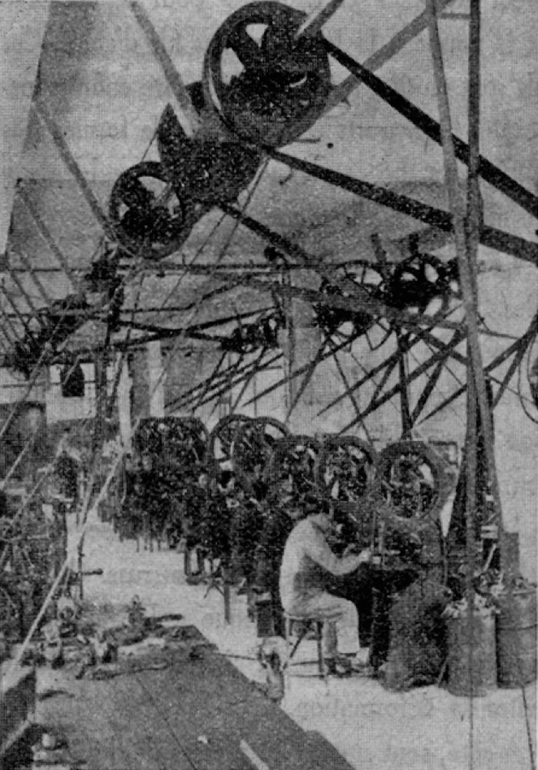 The metal stamping shop at Tron et Cie in 1935, a line of belt driven flywheel presses hung from overhead lineshafting with an operator seated at the nearest machine