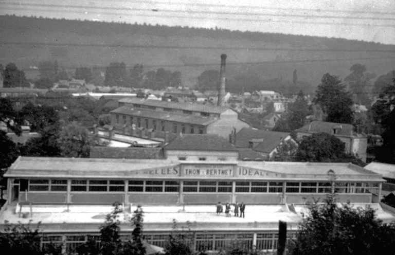 Elevated view of the Tron et Berthet works after the 1948 alterations, a long glazed hall lettered Selles Tron & Berthet Idéale across its fascia with the town and chimney behind