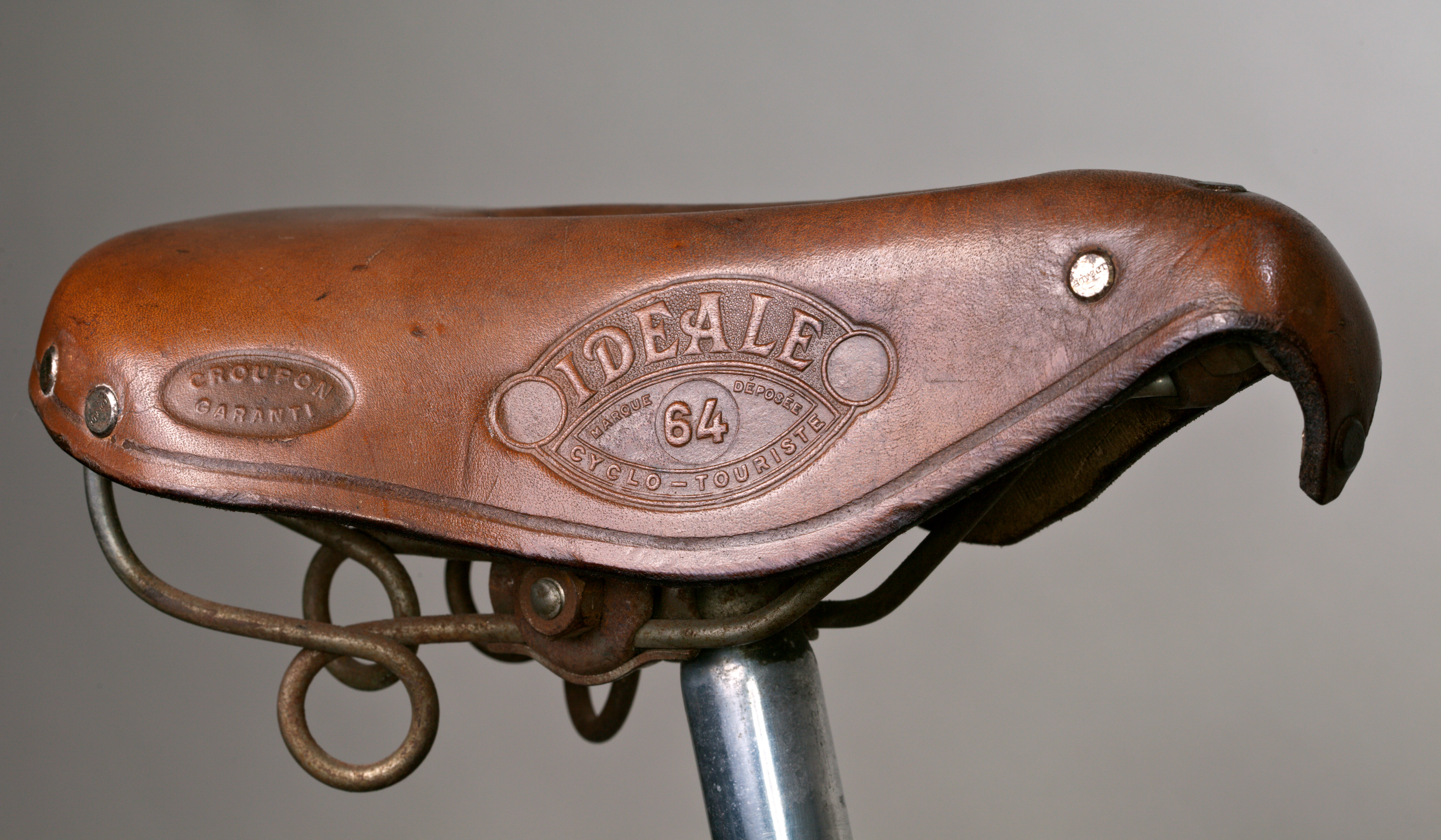 An Idéale 64 Cyclo-Touriste in tan leather on a chrome seatpost, its hawk bill nose and Croupon Garanti oval catching the light above the coiled rear springs