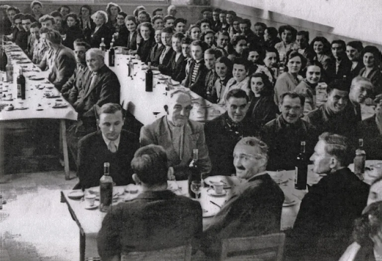 The inauguration of the works canteen at Idéale, staff seated the length of long tables set with wine bottles and cups, faces turned toward the camera