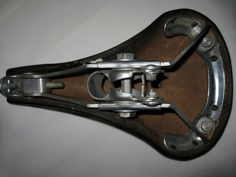 Underside of an Idéale saddle showing the alloy undercarriage and tension bolt slung between the chrome rear tabs riveted through the hide