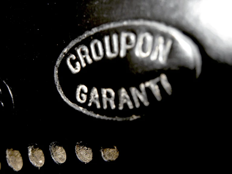 Sharp macro of the Croupon Garanti oval pressed into black leather, its letters catching the light above a row of silvered rivets