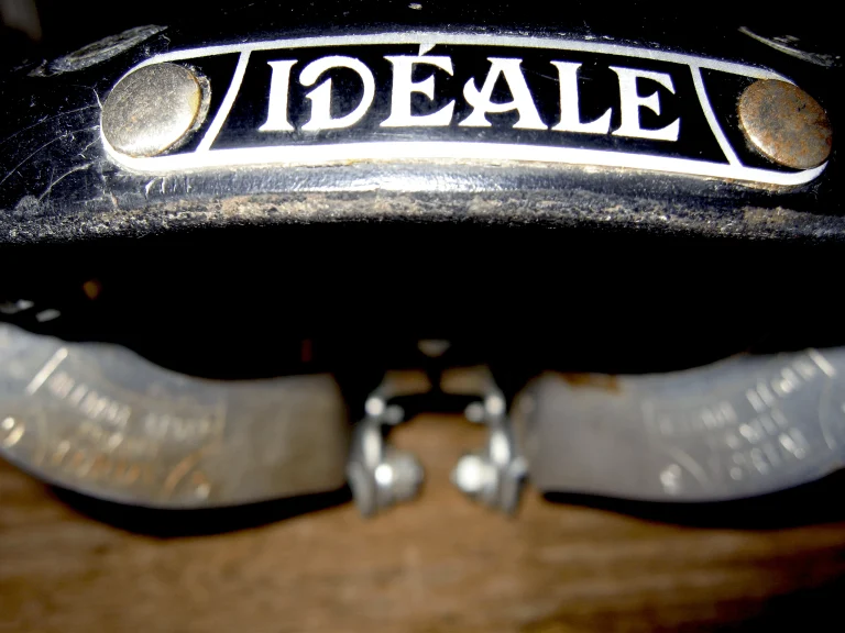 The enameled Idéale nose plate riveted to a saddle, with the polished alloy clamp bands visible below in the shadow