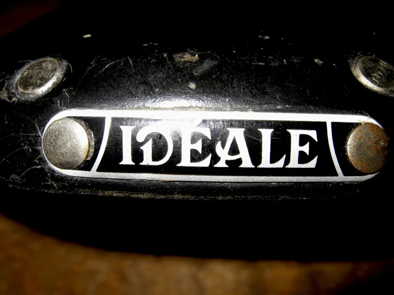 Tight macro of the enameled Idéale nose plate, its white letters on black held by two dome rivets in scuffed leather