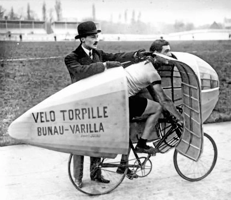 Marcel Berthet crouched inside the Vélo Torpille Bunau-Varilla, a fully faired streamliner held upright at the trackside by a man in a bowler hat