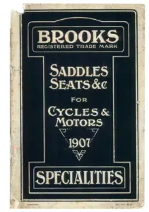 Black printed card catalog cover lettered in cream within a ruled Art Nouveau border, reading BROOKS, REGISTERED TRADE MARK, SADDLES SEATS and c, FOR CYCLES and MOTORS, 1907, SPECIALITIES, with COPYRIGHT and ENT. STA. HALL. at the foot. The card is rubbed and chipped along the spine edge.