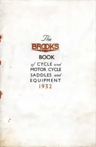 Cream card catalog cover, foxed and stained at the edges, with the lettering centred in the upper half. The word BROOKS is set in the house wedge-shaped red logotype with REGISTERED TRADE MARK beneath it, preceded by the word The in a script face. Below, in black capitals, BOOK of CYCLE and MOTOR CYCLE SADDLES and EQUIPMENT, with the year 1932 in red at the foot.