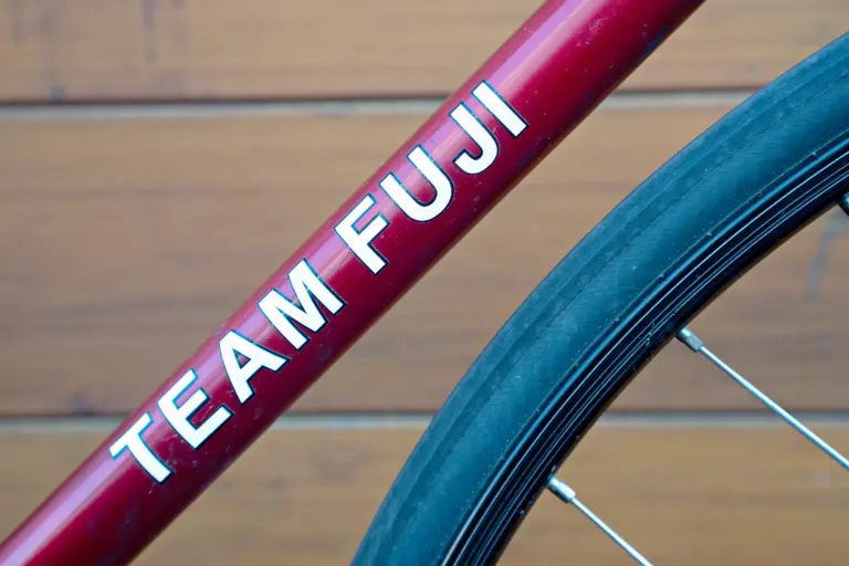 Close view of the TEAM FUJI down tube decal in white on the metallic red frame