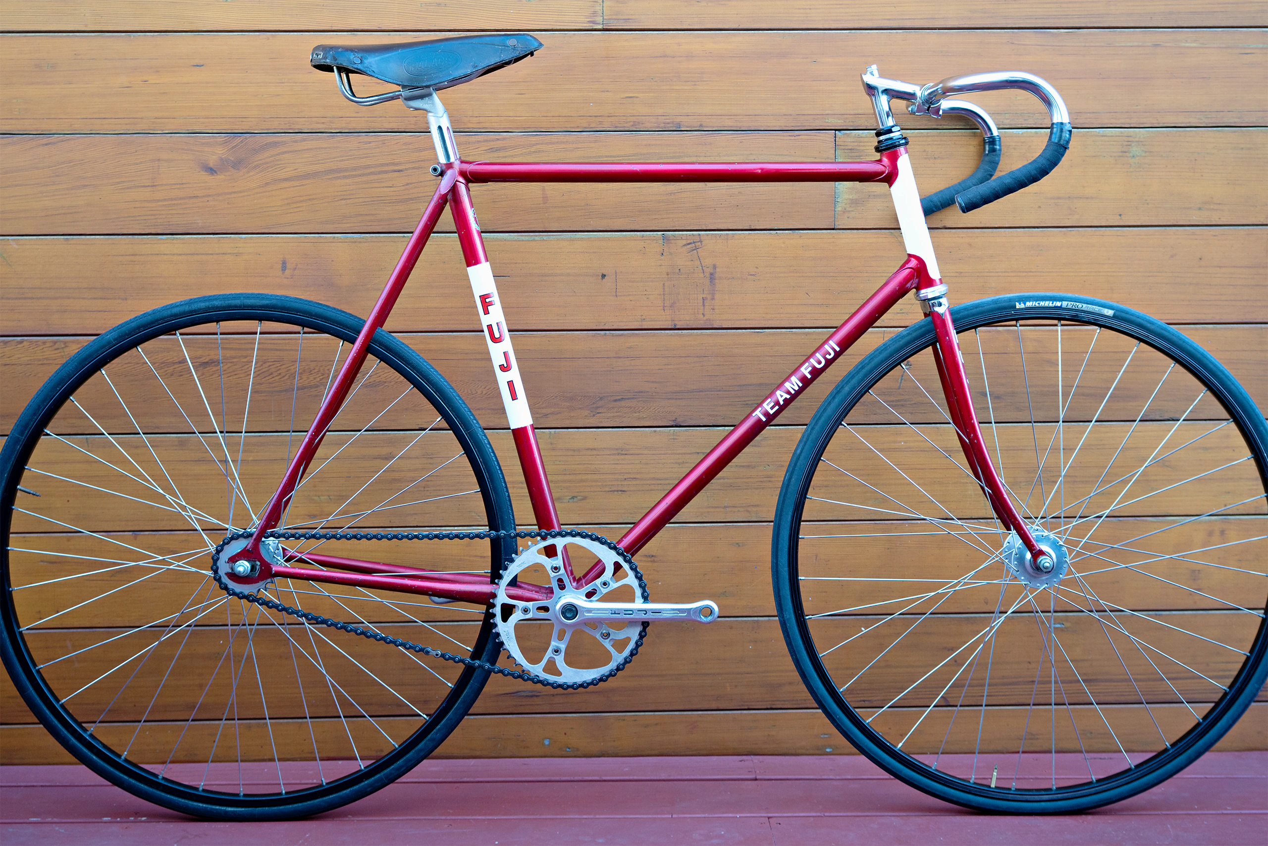 Drive-side profile of a 1970s Team Fuji track bicycle in metallic red with white head tube and seat tube panels, fitted with a Sugino crankset, Araya rims and a Palace leather saddle