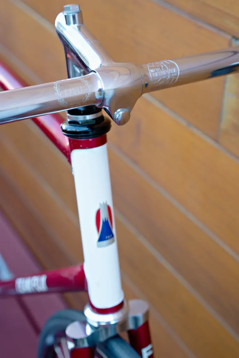 Mount Fuji head badge on the white head tube panel of the Team Fuji, with the Nitto Olympiade stamp and the Fuji laurel engraving on the handlebar above it