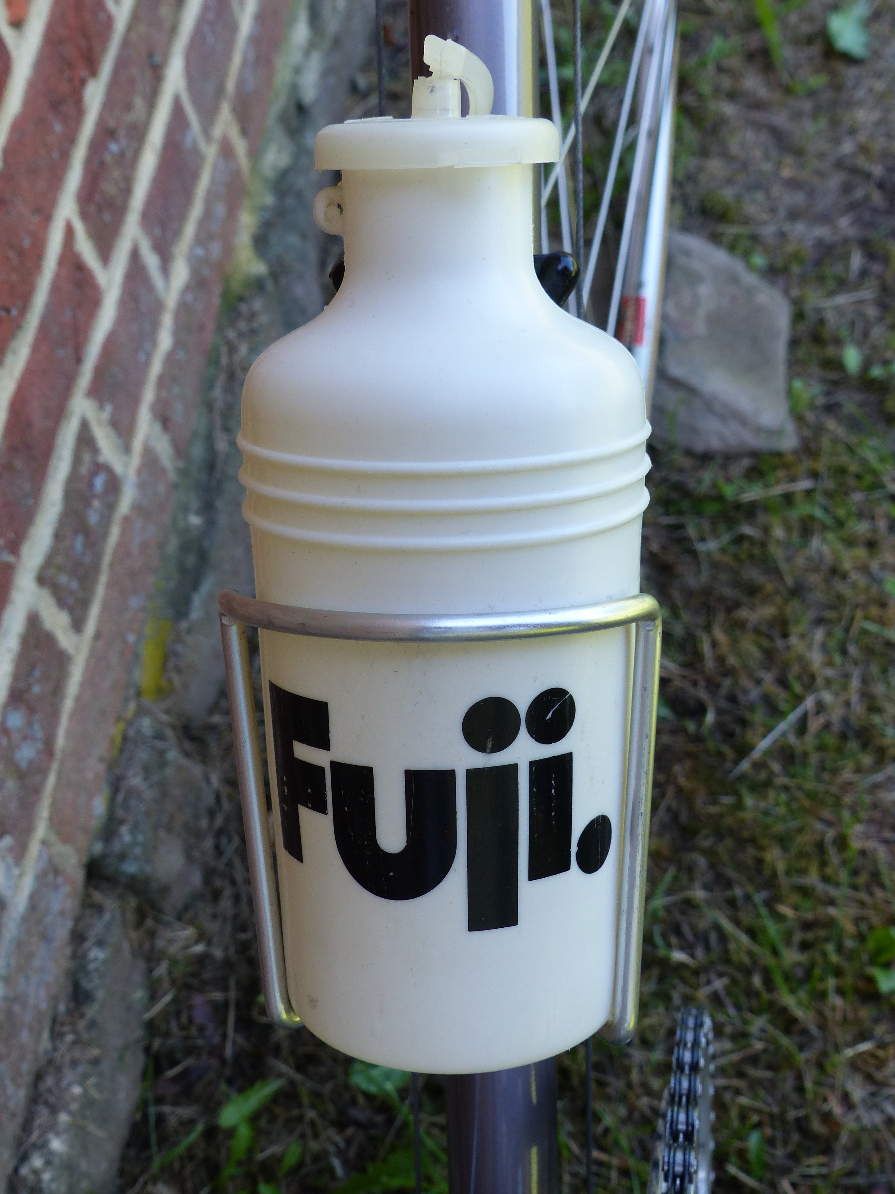 Cream plastic water bottle carrying the 1970s Fuji wordmark in black, held in a chrome wire cage on a bicycle down tube