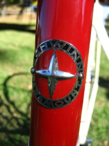 Round Schwinn Paramount head badge on a red head tube, with a raised chrome four-point star inside a black ring lettered SCHWINN PARAMOUNT