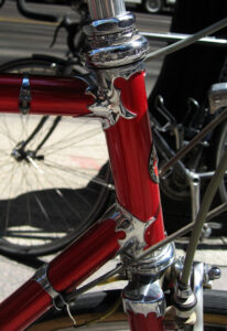 Close-up of a red Schwinn Paramount head tube showing chrome-plated ornate cut lugs at the top tube and down tube joints, above a Campagnolo headset