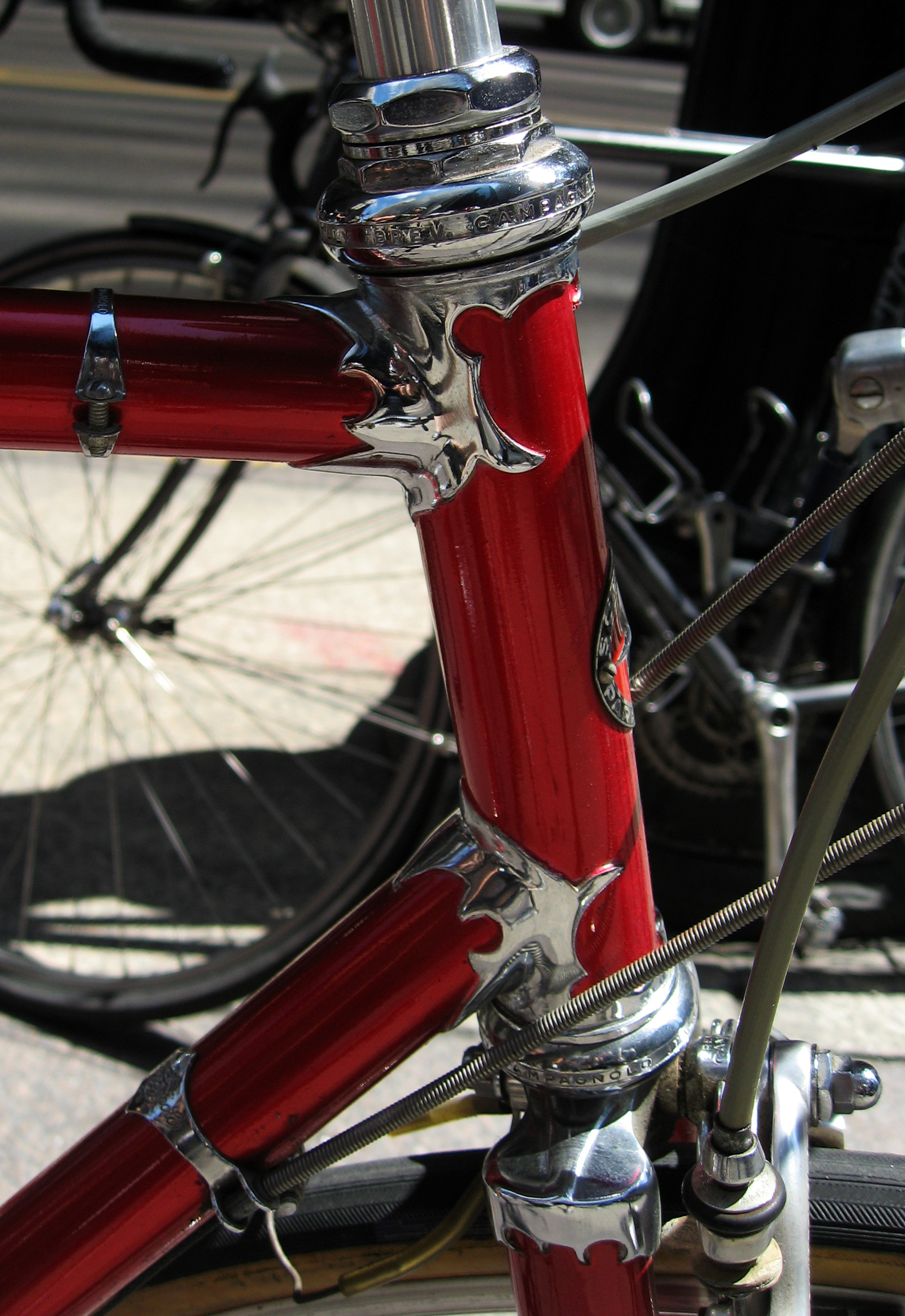 Close-up of a red Schwinn Paramount head tube showing chrome-plated ornate cut lugs at the top tube and down tube joints, above a Campagnolo headset