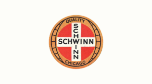 Circular Schwinn badge with a red field, a white cross lettered SCHWINN twice, and a tan outer ring reading QUALITY and CHICAGO, centered on a plain light ground