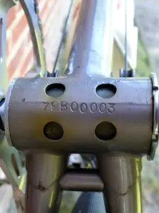 Underside of a bicycle bottom bracket shell stamped with the serial number 79B00003 above two drain holes, with a thread specification stamped around the shell edge