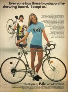 Magazine advertisement headed Everyone has these bicycles on the drawing board. Except us., showing a woman in a Fuji T-shirt standing behind a twelve-speed Fuji Royale, with a racer holding a second bicycle behind her