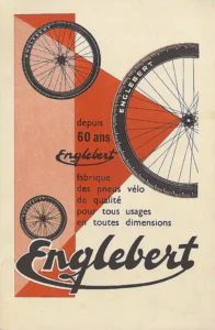 Englebert advertisement from Englebert Vélo-Magazine, November 1951, page 27: a drawing of three spoked bicycle wheels on Englebert-branded tires in different sizes, a large half wheel cut by the right edge and two smaller whole wheels to the left, set over interlocking red-orange and pale salmon triangles and panels on a cream ground.