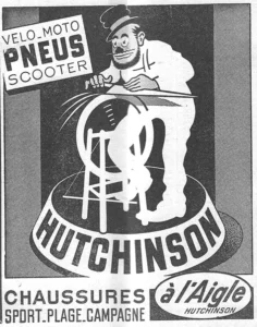 Hutchinson advertisement from L'Officiel du cycle, 22 June 1957, page 36: a bearded cartoon man in a small brimmed hat and spectacles, drawn like a street knife grinder, presses a long blade against a spinning wheel on a wooden stand, with streaks flying from the wheel, the whole set on a round drum that carries the HUTCHINSON name in heavy capitals.