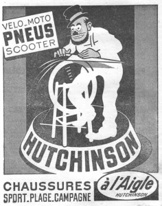 Hutchinson advertisement from L'Officiel du cycle, 13 April 1957: a bearded cartoon man in a small round cap leans over a bar as he pedals a frame built around a spinning tire, on a round drum that carries the firm's name, beside a white panel lettered for tires.