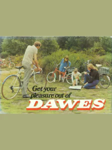 A photograph of a man astride a white drop-handlebar bicycle, two girls and a woman with small-wheel bicycles carrying plaid bags and a map spread on the grass, under the title in black and red and white letters.